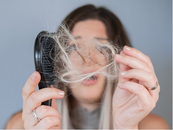Mladá žena si prohlíží padající vlasy v ruce – ilustrační foto k článku o návycích, které způsobují padání vlasů